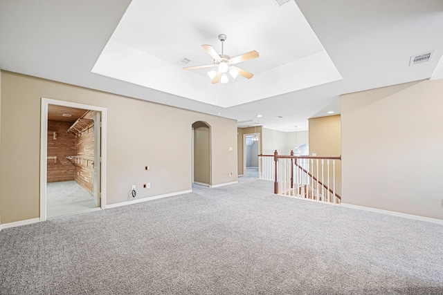 carpeted empty room featuring a raised ceiling, ceiling fan, and wood walls