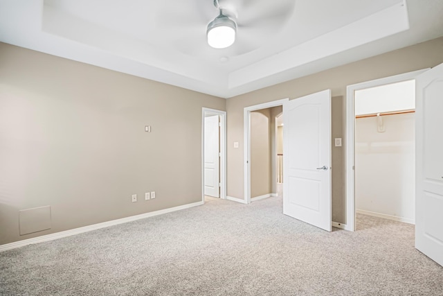 unfurnished bedroom with a closet, a tray ceiling, ceiling fan, and light colored carpet