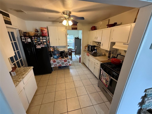 kitchen featuring light tile patterned floors, white cabinets, black refrigerator, and stainless steel gas range oven