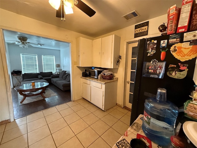 kitchen featuring light tile patterned floors, white cabinetry, and black fridge