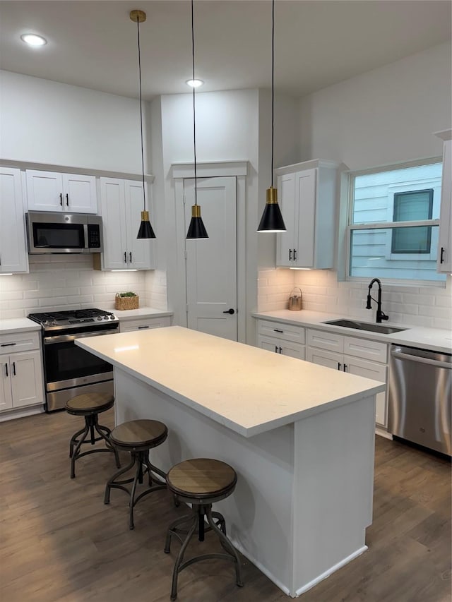 kitchen featuring stainless steel appliances, sink, white cabinetry, hanging light fixtures, and a kitchen island