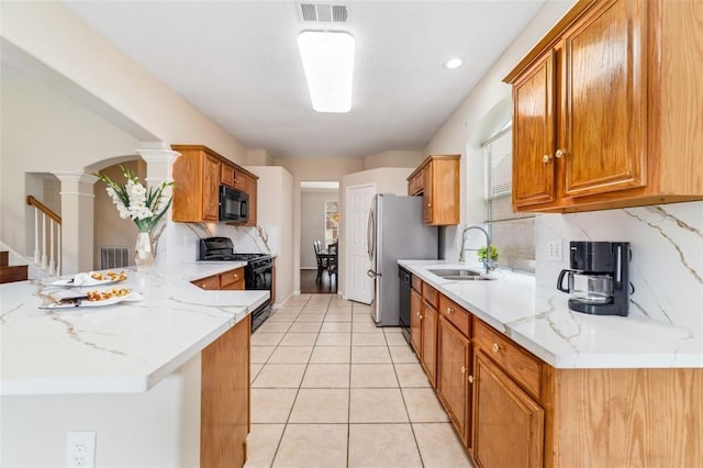 kitchen featuring kitchen peninsula, decorative columns, light stone counters, sink, and black appliances