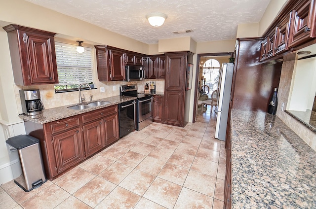 kitchen with sink, stainless steel appliances, dark stone counters, a textured ceiling, and light tile patterned flooring