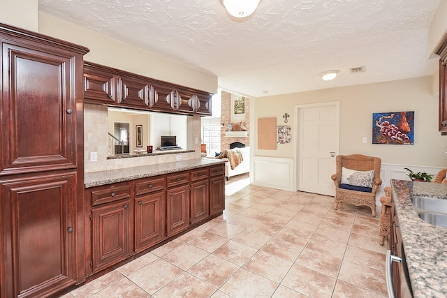 kitchen with sink, light stone countertops, a textured ceiling, a fireplace, and light tile patterned flooring