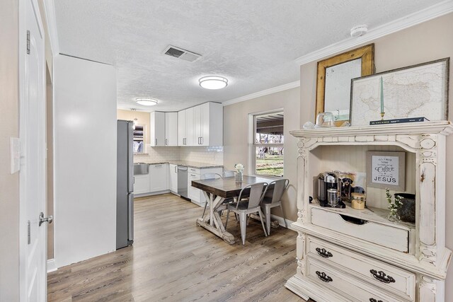 kitchen featuring stainless steel appliances, light hardwood / wood-style flooring, backsplash, a textured ceiling, and white cabinets