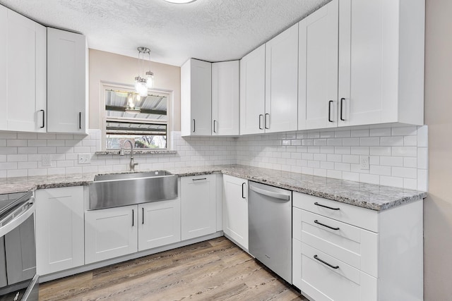 kitchen with light wood-type flooring, stainless steel dishwasher, sink, pendant lighting, and white cabinets