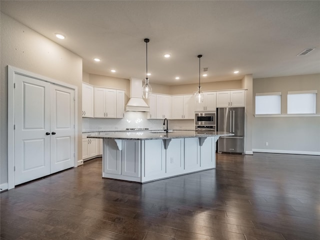 kitchen with a center island with sink, premium range hood, stainless steel appliances, and white cabinetry