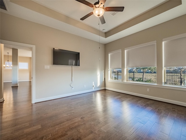 unfurnished room featuring ceiling fan with notable chandelier, dark wood-type flooring, and a raised ceiling