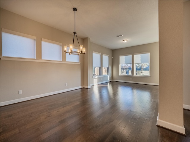 unfurnished living room featuring an inviting chandelier and dark hardwood / wood-style flooring