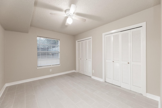 unfurnished bedroom with ceiling fan, a textured ceiling, and multiple closets