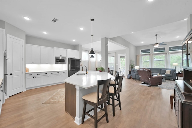 kitchen featuring fridge, stainless steel microwave, ceiling fan, a center island with sink, and hanging light fixtures