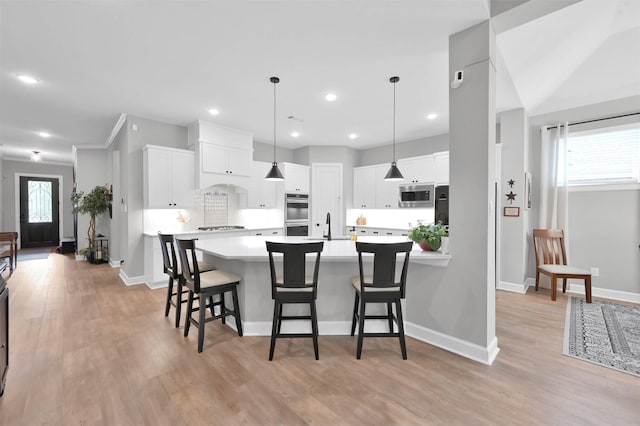 kitchen featuring appliances with stainless steel finishes, a breakfast bar, light hardwood / wood-style flooring, white cabinets, and hanging light fixtures