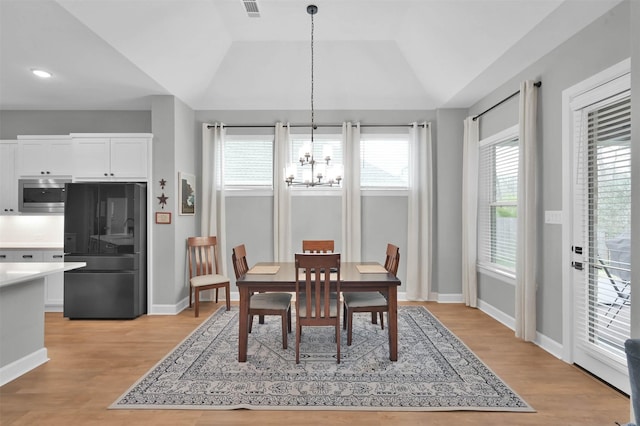 dining room featuring a chandelier, light hardwood / wood-style floors, a raised ceiling, and lofted ceiling