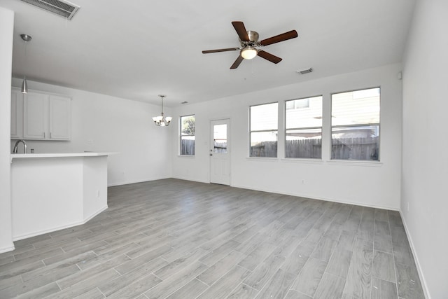 unfurnished living room featuring ceiling fan with notable chandelier and light wood-type flooring