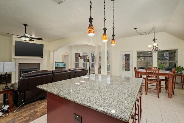 kitchen featuring light stone counters, ceiling fan with notable chandelier, decorative light fixtures, a center island, and a tiled fireplace