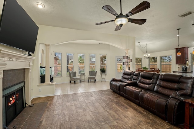 living room featuring ceiling fan with notable chandelier, lofted ceiling, a textured ceiling, and a tile fireplace