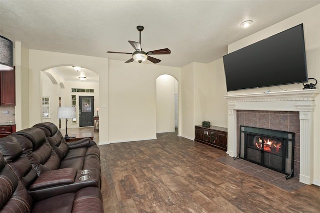 living room with a fireplace, a textured ceiling, dark hardwood / wood-style flooring, and ceiling fan