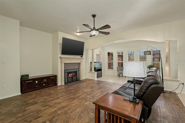 living room featuring decorative columns, hardwood / wood-style flooring, ceiling fan, and a tiled fireplace