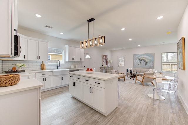 kitchen with backsplash, sink, decorative light fixtures, a center island, and white cabinetry