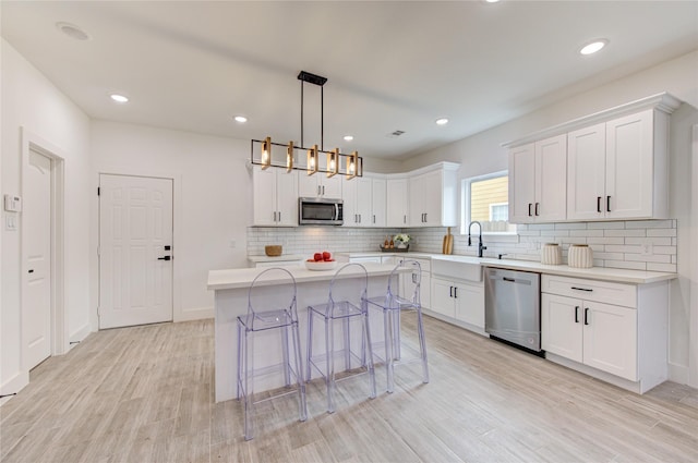 kitchen featuring sink, a center island, hanging light fixtures, white cabinets, and appliances with stainless steel finishes