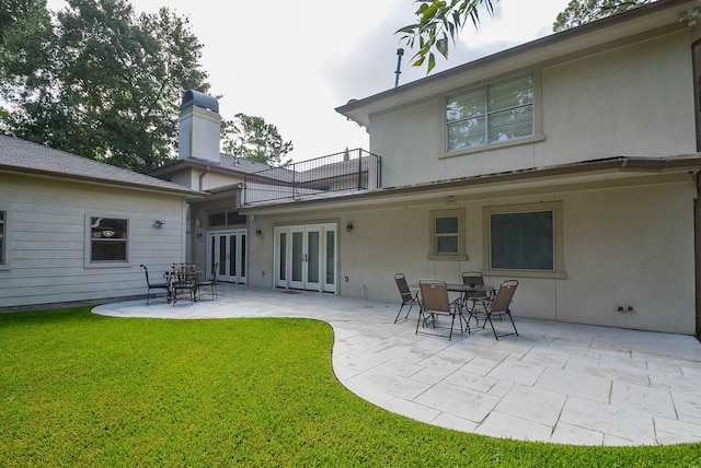 rear view of property featuring a balcony, a yard, a patio, and french doors