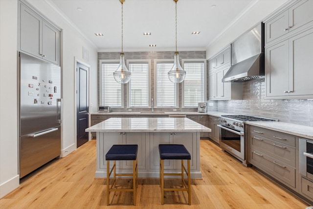 kitchen with light stone countertops, sink, wall chimney range hood, high quality appliances, and a kitchen island