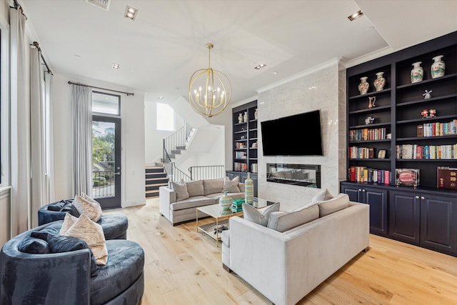 living room with ornamental molding, light hardwood / wood-style flooring, built in features, a chandelier, and a tiled fireplace