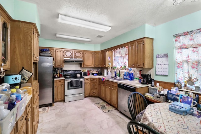 kitchen with stainless steel appliances, brown cabinets, light countertops, and under cabinet range hood