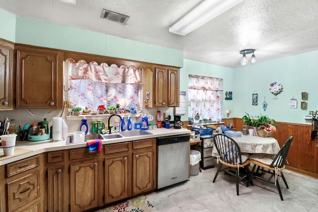 kitchen featuring visible vents, light countertops, stainless steel dishwasher, wainscoting, and brown cabinets