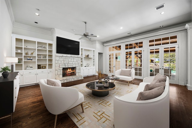 living room with french doors, a stone fireplace, ceiling fan, built in features, and ornamental molding