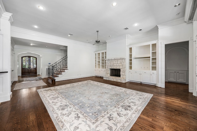 unfurnished living room with french doors, a stone fireplace, ceiling fan, built in features, and dark hardwood / wood-style flooring