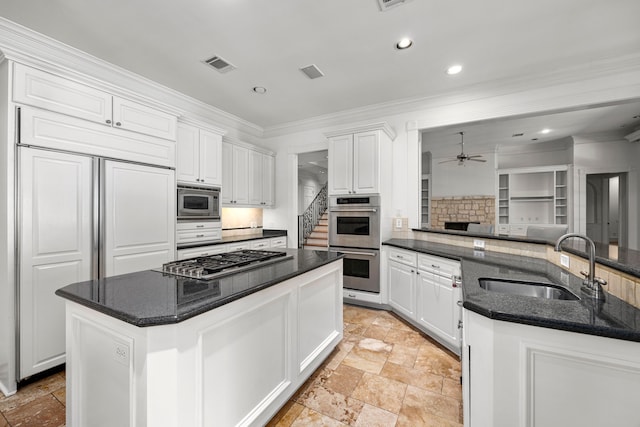 kitchen featuring a center island with sink, sink, built in appliances, tasteful backsplash, and white cabinetry