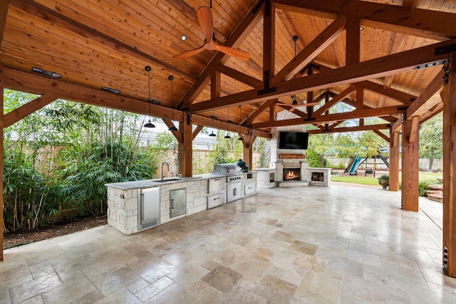 view of patio featuring ceiling fan, sink, exterior kitchen, an outdoor stone fireplace, and a gazebo