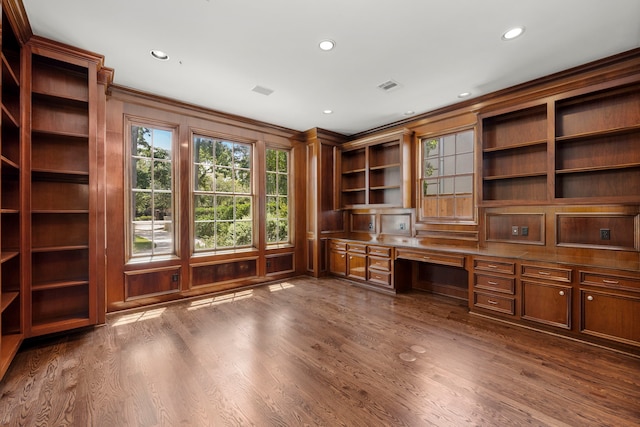 unfurnished office featuring wood walls, built in desk, dark wood-type flooring, and ornamental molding