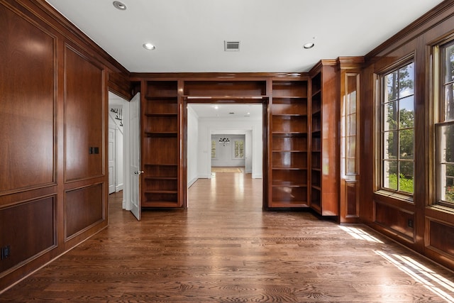 interior space with dark wood-type flooring, built in features, a healthy amount of sunlight, and wood walls