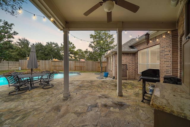 patio terrace at dusk featuring a fenced in pool, grilling area, and ceiling fan