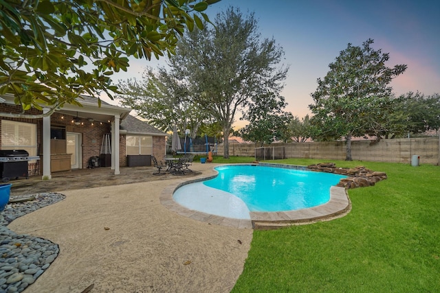 pool at dusk with a yard, a patio, a trampoline, and a grill