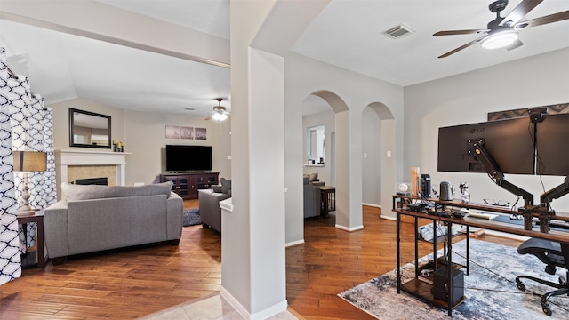 home office featuring a tiled fireplace, ceiling fan, wood-type flooring, and vaulted ceiling