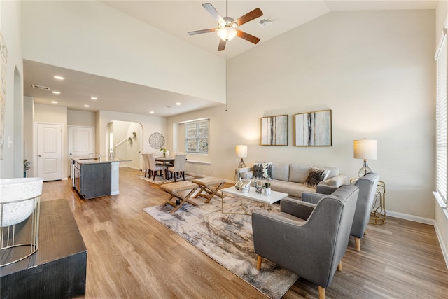 living room with ceiling fan, sink, lofted ceiling, and light wood-type flooring