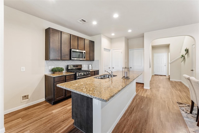 kitchen with light stone countertops, sink, a center island with sink, appliances with stainless steel finishes, and light wood-type flooring