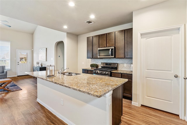 kitchen with dark brown cabinetry, sink, a kitchen island with sink, stainless steel appliances, and decorative backsplash