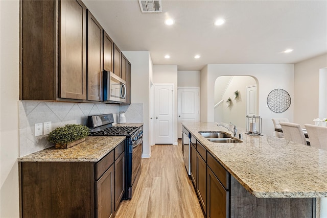 kitchen with sink, stainless steel appliances, light stone counters, light hardwood / wood-style floors, and a center island with sink