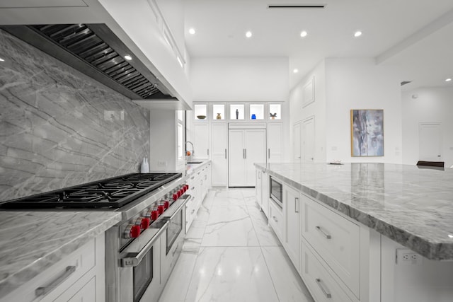 kitchen featuring white cabinets, appliances with stainless steel finishes, premium range hood, and light stone countertops