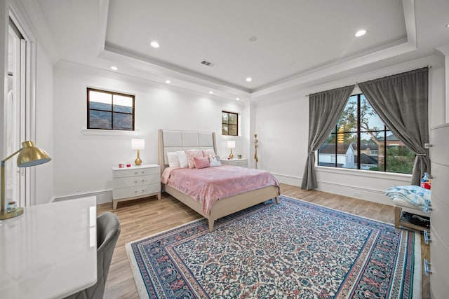 bedroom with a tray ceiling and light wood-type flooring