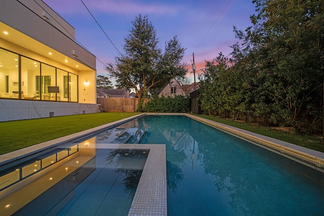 pool at dusk featuring a lawn