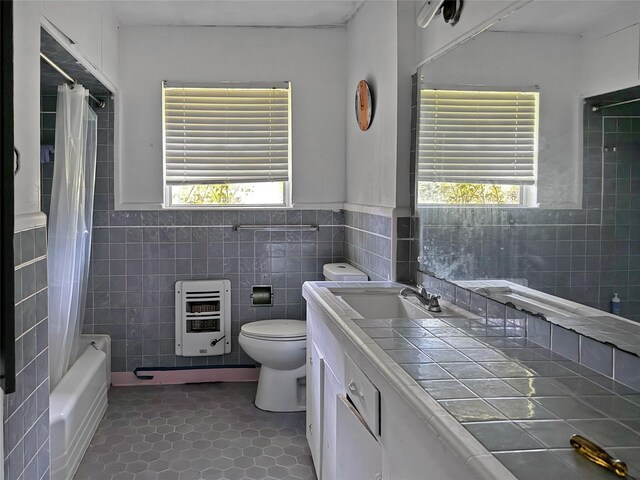 full bathroom featuring tile patterned floors, heating unit, a healthy amount of sunlight, and tile walls