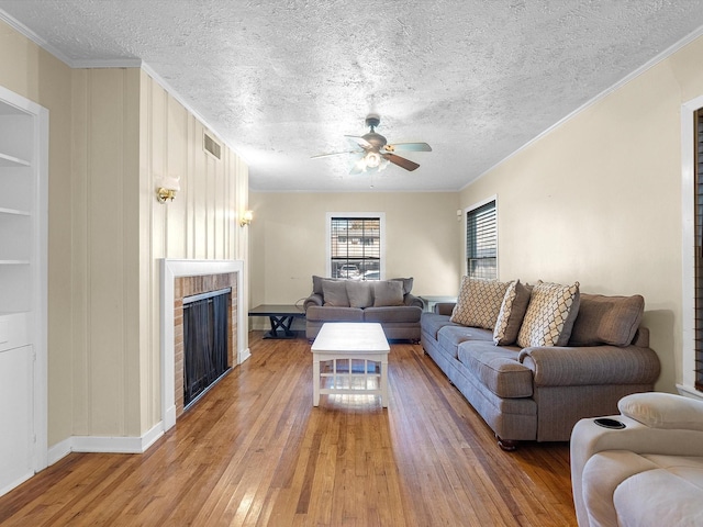 living room with ceiling fan, wood-type flooring, a textured ceiling, a fireplace, and ornamental molding