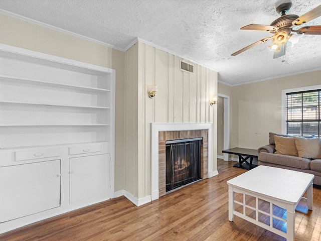 living room featuring ornamental molding, built in shelves, a textured ceiling, hardwood / wood-style flooring, and a fireplace