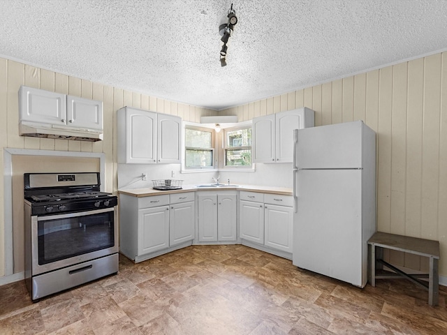 kitchen with wooden walls, sink, white cabinetry, white fridge, and stainless steel range with gas cooktop