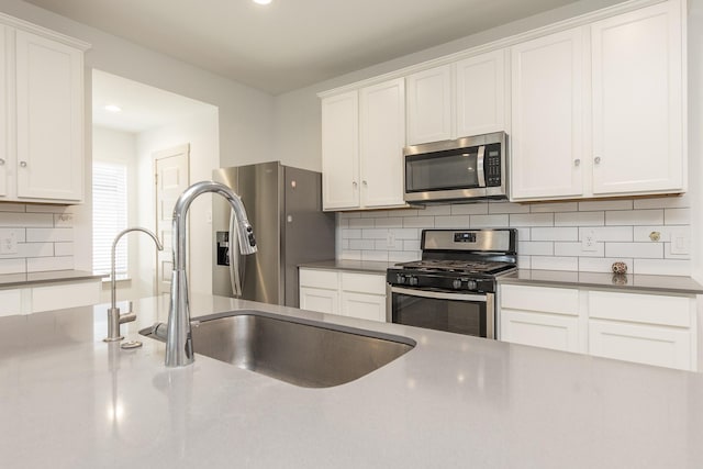 kitchen featuring decorative backsplash, appliances with stainless steel finishes, white cabinetry, and sink